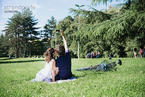 Rückansicht eines Paares  das im Park sitzend ein Smartphone mit sich führt  Arezzo  Toskana  Italien