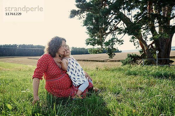 Schwangere Frau sitzt im Feld mit Kleinkind auf dem Schoss