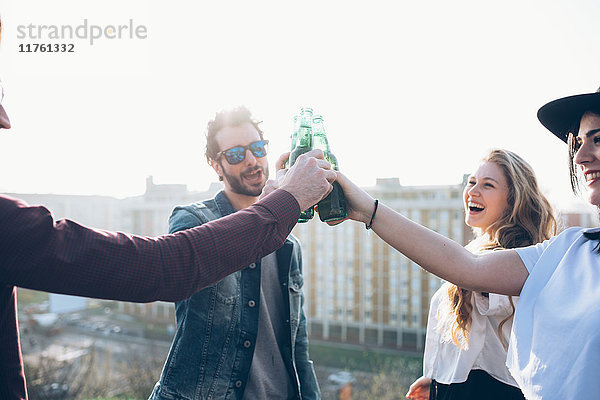 Gruppe von Freunden genießt Dachparty  hält Bierflaschen in der Hand  macht Toast