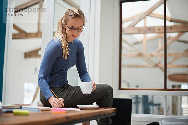 Designerin schreibt Notizen  während sie auf dem Schreibtisch des Designstudios sitzt