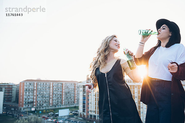Zwei junge Frauen  auf dem Dach  trinken Flaschenbier