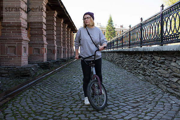 Junge Frau mit BMX-Fahrrad in gepflasterter Straße