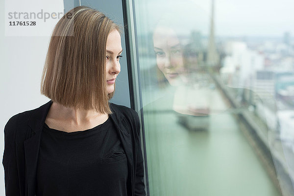 Junge Geschäftsfrau schaut durch ein Bürofenster