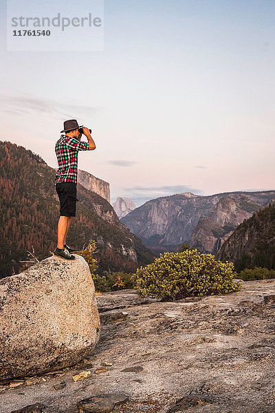 Mann steht auf einem Felsblock und schaut durch ein Fernglas  Yosemite National Park  Kalifornien  USA