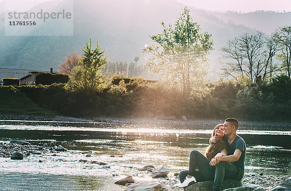 Romantisches Paar sitzt auf Felsen am Fluss und lächelt