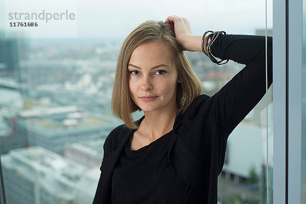 Porträt einer selbstbewussten jungen Geschäftsfrau  die sich an den Fensterrahmen eines Büros lehnt