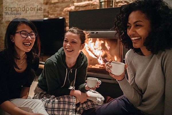 Freunde vor dem Feuer beim Kaffeetrinken lächelnd