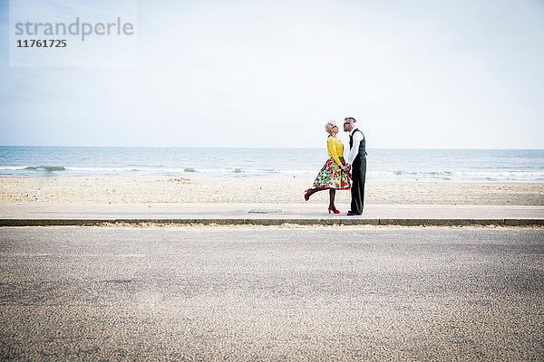 Ehepaar im Vintage-Stil der 1950er Jahre  das sich am Strand an den Händen hält