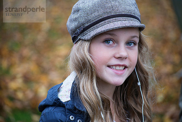 Porträt eines blonden Mädchens mit Bäckerjungenmütze  das über Kopfhörer Musik hört