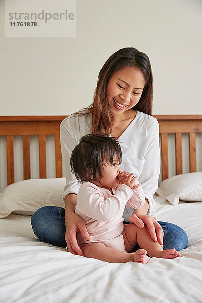 Frau mit gekreuzten Beinen auf Bett mit Baby-Tochter