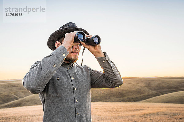 Mann schaut durch ein Fernglas auf sanfte Präriehügel  Bakersfield  Kalifornien  USA