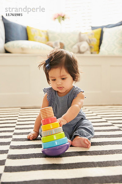 Auf dem Teppich sitzendes Mädchen spielt mit Babyspielzeug