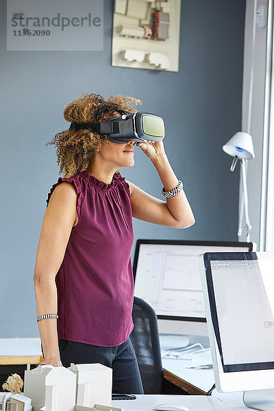 Architektin blickt durch ein Virtual-Reality-Headset am Büroschreibtisch