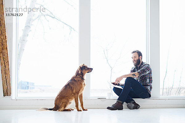 Junger männlicher Designer mit Hund im Designstudio Fenstersitz