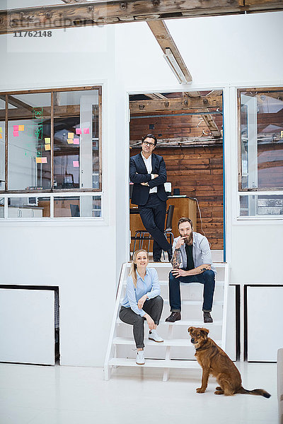 Porträt eines männlichen und weiblichen Designteams mit Hund auf der Treppe des Designstudios
