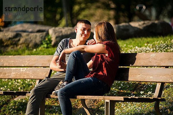 Paar sitzt auf einer Parkbank  von Angesicht zu Angesicht  lächelnd
