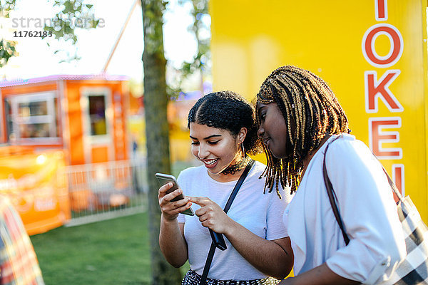 Zwei Mädchen auf der Kirmes  die sich ein Smartphone anschauen