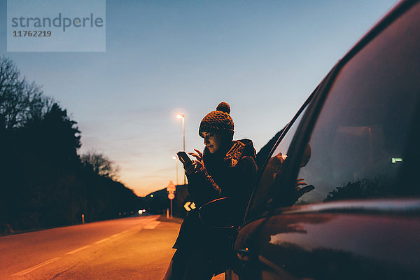 Frau  die in der Abenddämmerung am Straßenrand ein Smartphone betrachtet  Monte San Primo  Italien