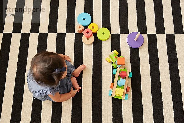 Draufsicht eines auf dem Teppich sitzenden Mädchens  das mit einer Spielzeugeisenbahn spielt