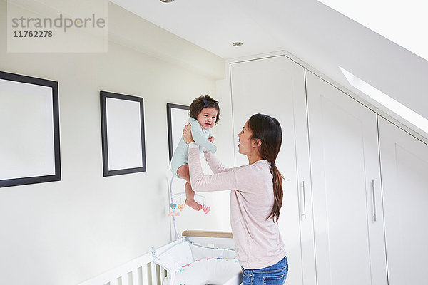 Glückliche Frau im mittleren Erwachsenenalter hält ihre kleine Tochter über dem Kinderbett