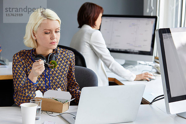 Designerin schaut während des Arbeitsessens am Büroschreibtisch auf den Laptop