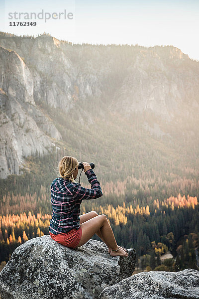 Frau sitzt auf einem Felsblock und schaut durch ein Fernglas hinaus  Yosemite National Park  Kalifornien  USA