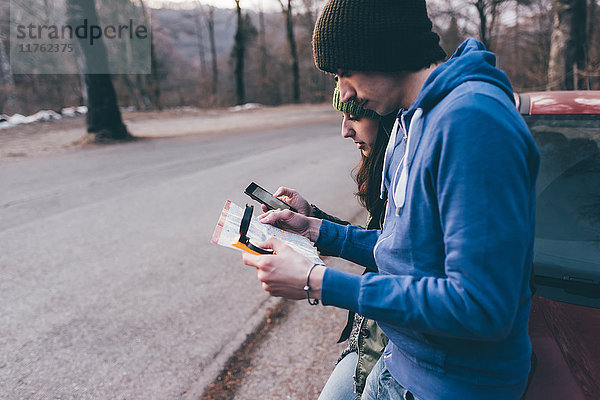 Wandererpaar beim Blick auf Karte und Smartphone am Waldwegrand  Monte San Primo  Italien