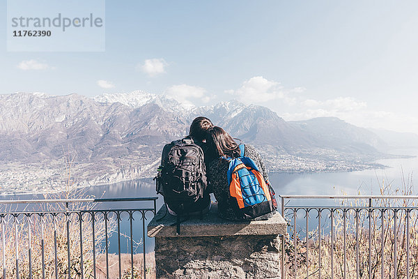 Rückansicht eines Paares  das auf einer Terrassenwand über dem Bergseeufer sitzt  Monte San Primo  Italien