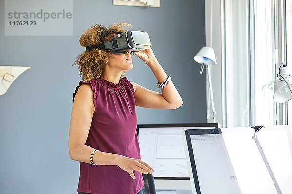 Architektin blickt durch ein Virtual-Reality-Headset am Büroschreibtisch