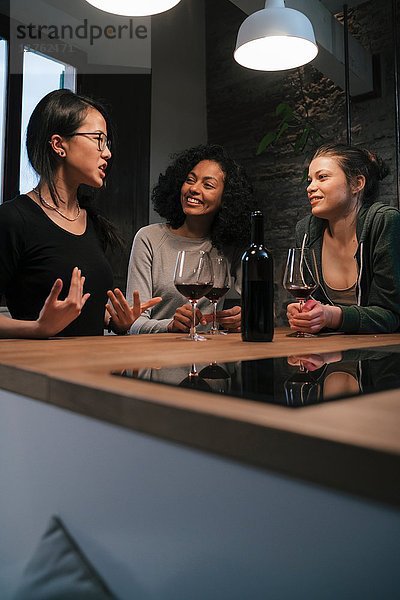 Freunde sitzen am Küchentisch und trinken Wein