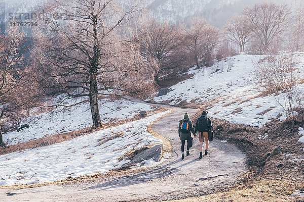 Rückansicht eines Wanderpaares  das auf einer verschneiten Landstraße wandert  Monte San Primo  Italien