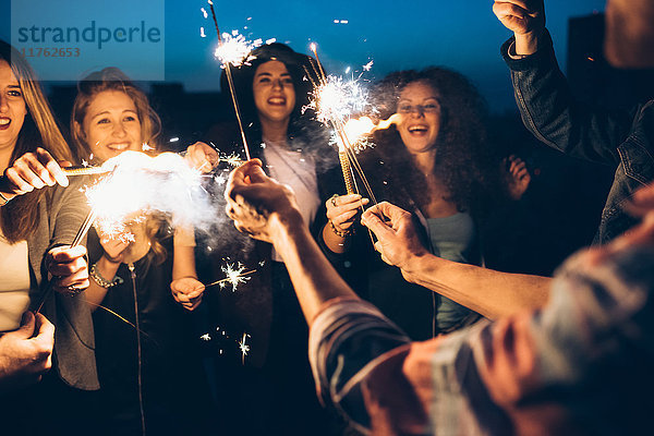 Eine Gruppe von Freunden genießt eine Dachparty und hält brennende Wunderkerzen