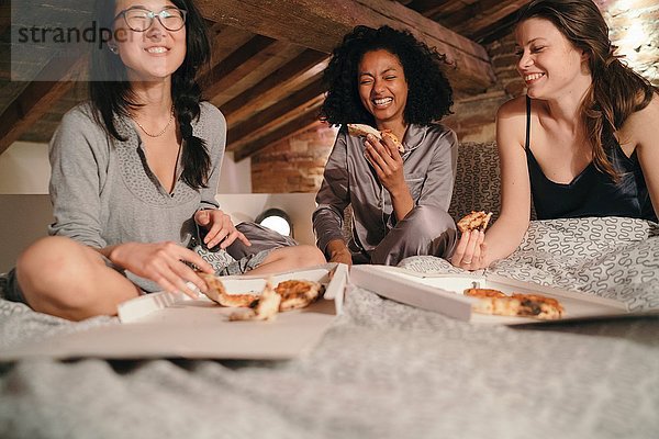 Mädchen sitzen im Bett und essen Pizza