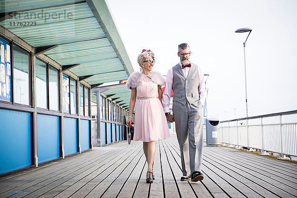 Ehepaar aus den 1950er Jahren im Vintage-Stil beim Spaziergang und Händchenhalten am Pier