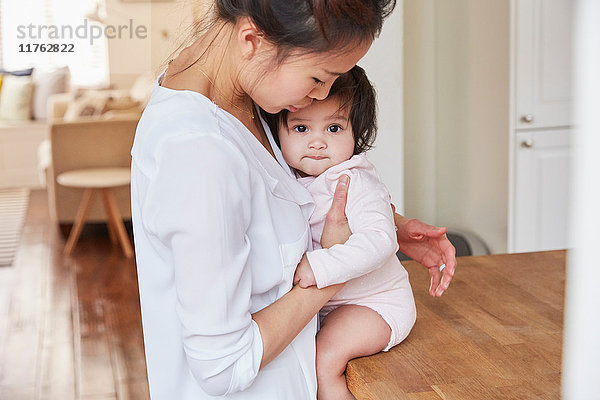 Frau umarmt Baby-Tochter auf Küchentheke
