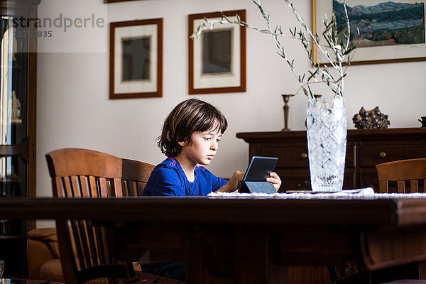 Junge sitzt am Tisch und benutzt Touchscreen auf digitalem Tablett