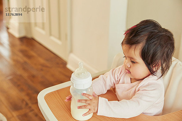 Mädchen hält Babymilchflasche auf Hochstuhl