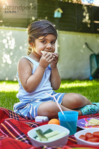 Porträt eines jungen Mädchens  das im Garten picknickt und ein Sandwich isst