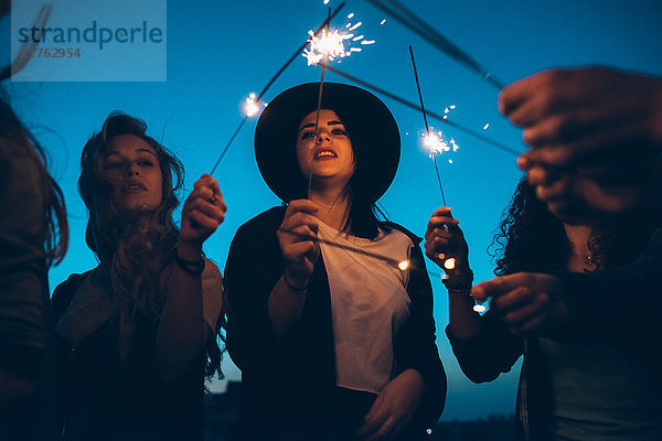 Eine Gruppe von Freunden genießt eine Dachparty und hält brennende Wunderkerzen