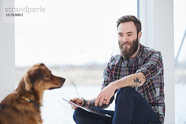 Junger männlicher Designer mit Hund im Designstudio Fenstersitz