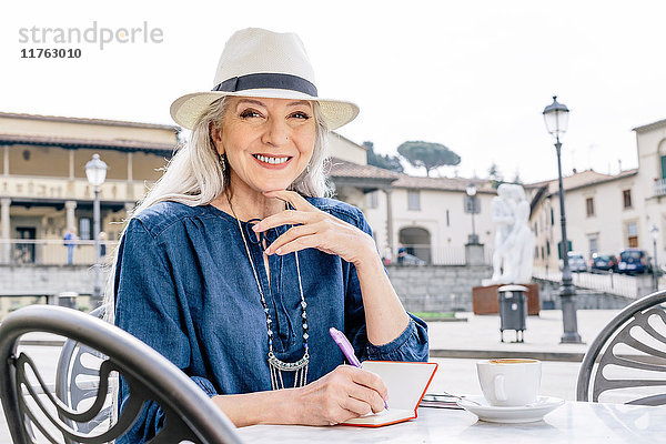 Porträt einer reifen Frau  die in ein Notizbuch schreibt  im Bürgersteig-Café  Fiesole  Toskana  Italien