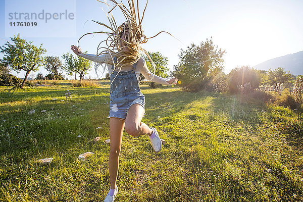 Lustige junge Frau mit langen geflochtenen blonden Haaren springt vor Freude im Feld herum  Mallorca  Spanien