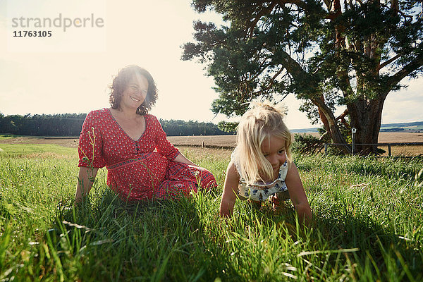 Schwangere Frau sitzt auf dem Feld mit einem Kleinkind  dessen Tochter im Gras krabbelt