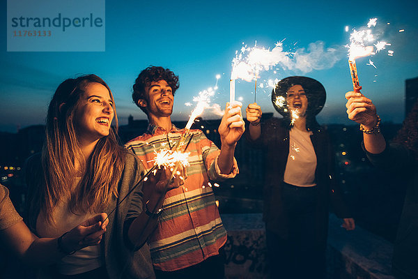 Eine Gruppe von Freunden genießt eine Dachparty und hält brennende Wunderkerzen