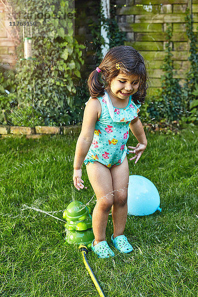 Junges Mädchen spielt im Garten  neben Wassersprinklern