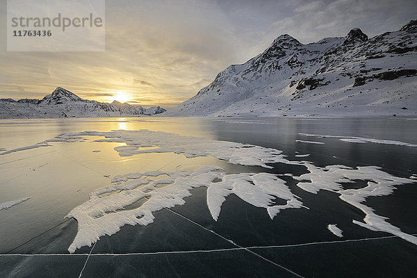 Die gefrorene Oberfläche des Lago Bianco umrahmt von schneebedeckten Gipfeln in der Morgendämmerung  Berninapass  Kanton Graubünden  Engadin  Schweiz  Europa