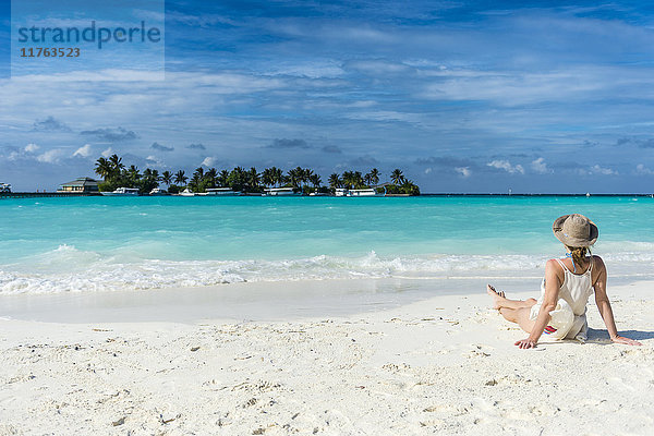 Frau sitzt an einem weißen Sandstrand und genießt das türkisfarbene Wasser  Sun Island Resort  Insel Nalaguraidhoo  Ari-Atoll  Malediven  Indischer Ozean  Asien