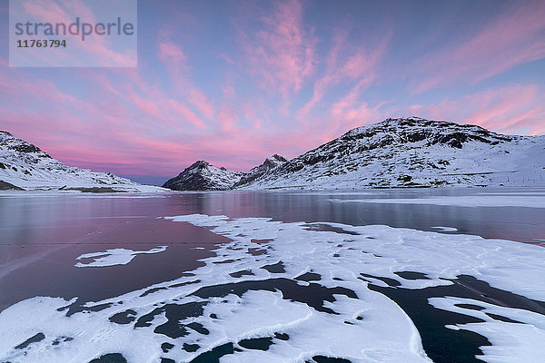 Der zugefrorene Lago Bianco umrahmt von rosa Wolken in der Morgendämmerung  Berninapass  Kanton Graubünden  Engadin  Schweiz  Europa