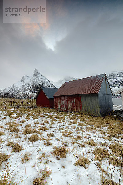 Wolken auf schneebedeckten Gipfeln über einer typischen Holzhütte namens Rorbu  Senja  Ersfjord  Provinz Troms  Norwegen  Skandinavien  Europa