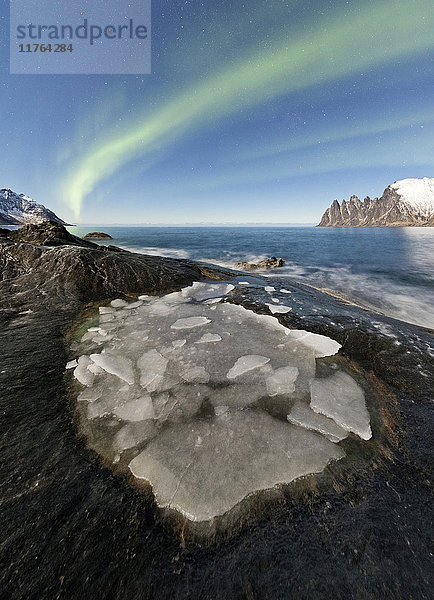 Das Nordlicht (Aurora borealis) beleuchtet die felsigen Gipfel und das eisige Meer in der Polarnacht  Tungeneset  Senja Troms  Norwegen  Skandinavien  Europa